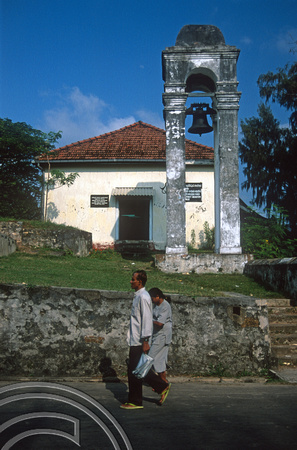 T15071. Locals walk past a bell tower built by the Dutch in 1701. Galle. Sri Lanka. 13.01.2002