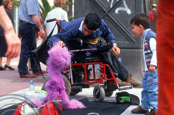 T15270. Busker in a wheelchair entertains a young boy. Port Olimpic. Barcelona. Spain. 18.04.2003