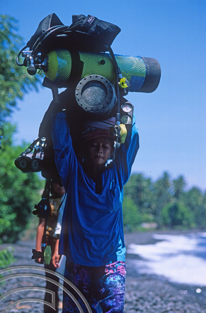 T8011. Young woman carrying scuba tanks. Tulamben. Bali. Indonesia. 25th October 1998